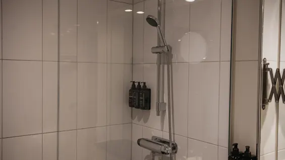 Ett modernt duschutrymme med vita kaklade väggar, ett kromfärgat duschhuvud och väggmonterade dispensrar för toalettartiklar.