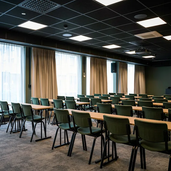 Et romslig konferanserom med rader av bord og stoler, klart for et møte eller en presentasjon.