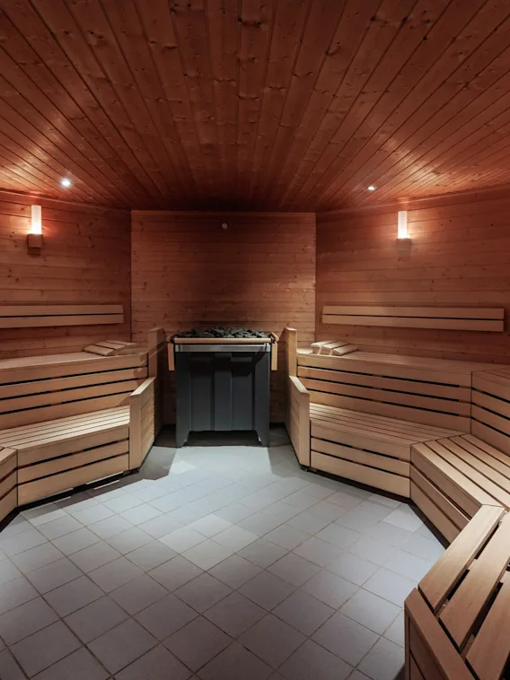 En tresauna med benker som omgir en sentral varmeapparat med steiner, opplyst av myke vegglamper som skaper en varm og innbydende atmosfære.