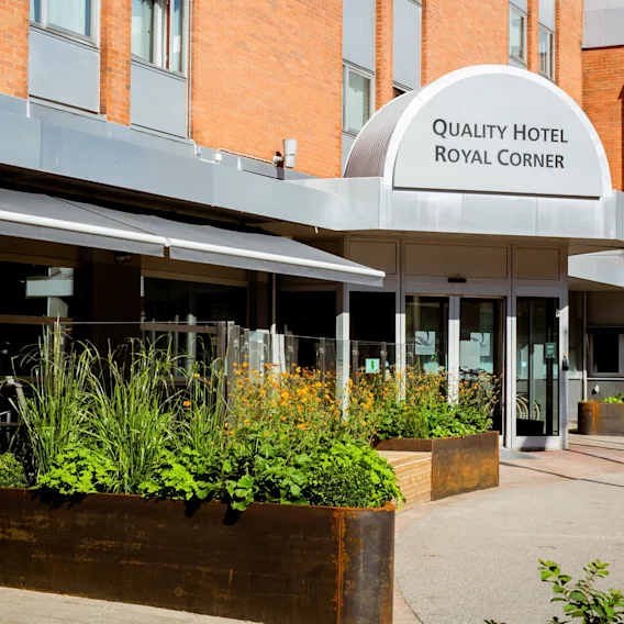 Den inbjudande entrén till Quality Hotel Royal Corner, med frodiga gröna planteringar och en uteservering under en markis.