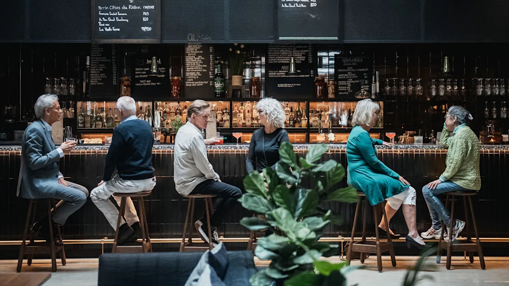 People conversing at a bar with drinks, in a sophisticated setting with menus on blackboards.