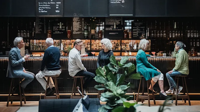 People conversing at a bar with drinks, in a sophisticated setting with menus on blackboards.