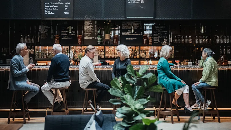 People conversing at a bar with drinks, in a sophisticated setting with menus on blackboards.