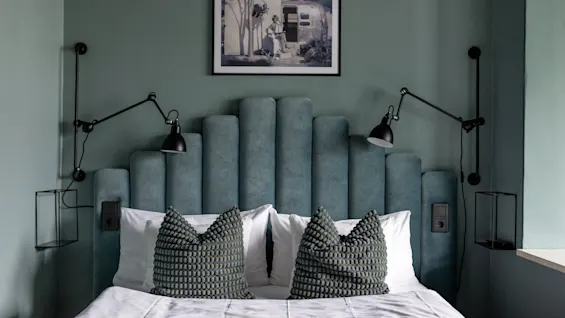 Et komfortabelt soverom med en teksturert sengegavl, stemningsfull belysning og et innrammet bilde av en person som slapper av utendørs.