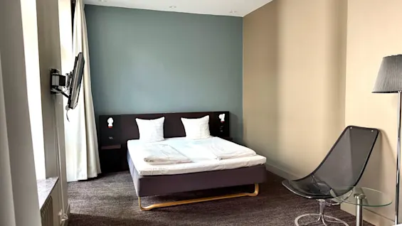 Ett modernt och bekvämt hotellrum med en säng, en stol och en TV, med en tvåfärgad väggdesign.