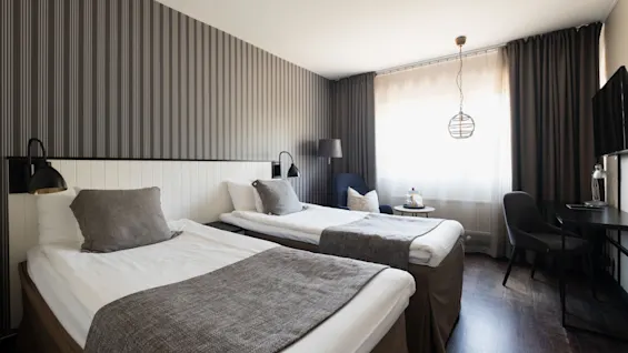 Et moderne hotelværelse med to komfortable senge, et skrivebord og et lyst vindue, perfekt til et afslappende ophold.