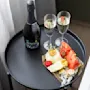 Et lite bord dekket for feiring, med en flaske prosecco og to glass fylt med bobler. Et fargerikt fat med fersk frukt og snacks gir en følelse av luksus.