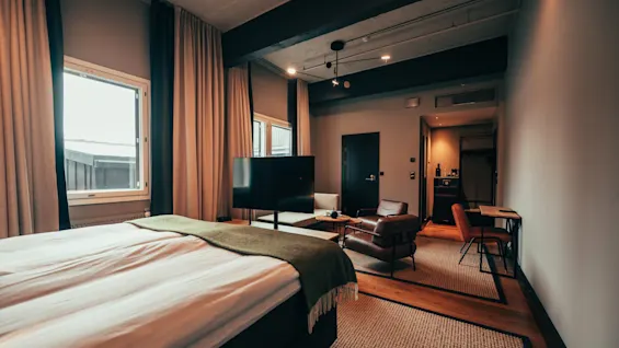 A spacious and comfortable hotel room with a large bed, a separate seating area with a TV, and a small dining or work table.