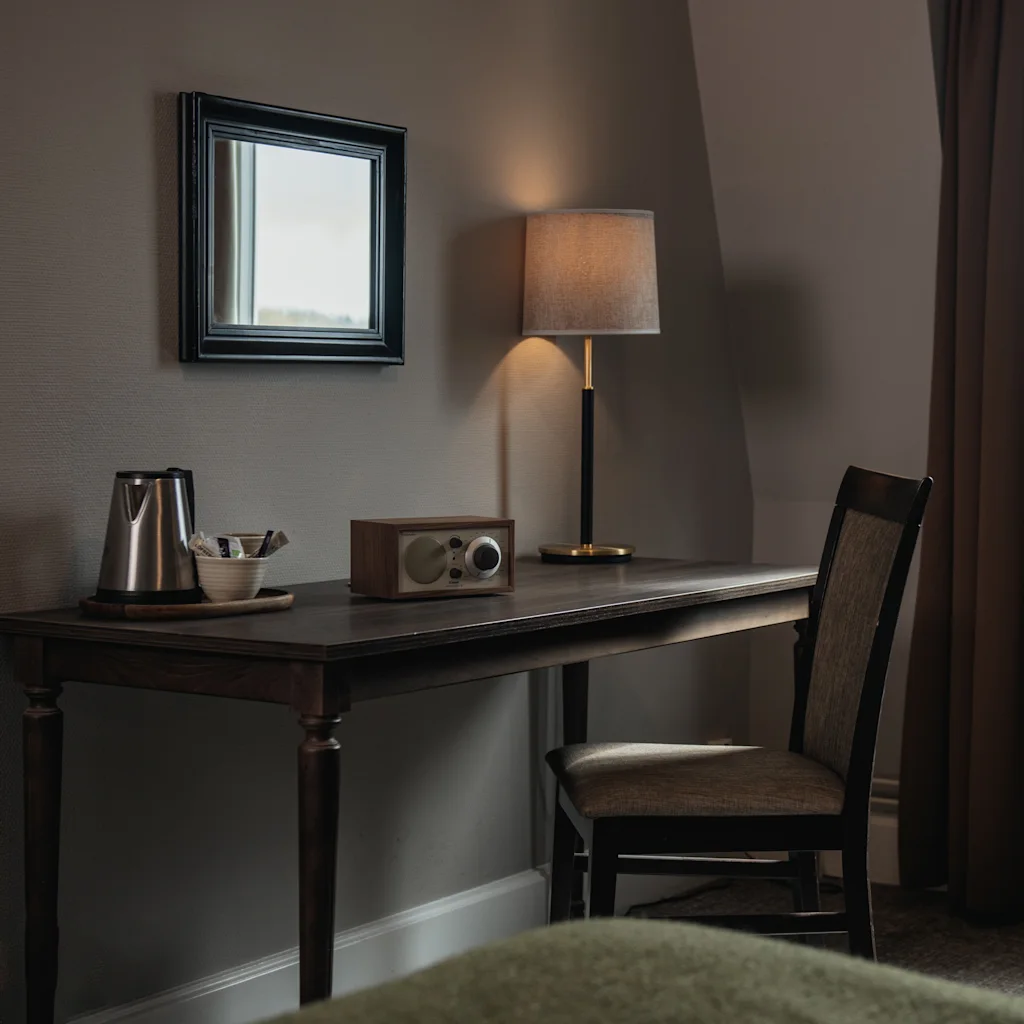 Et komfortabelt hotelværelse på Home Hotel Uman med et skrivebord, lampe og tefaciliteter, badet i naturligt lys.