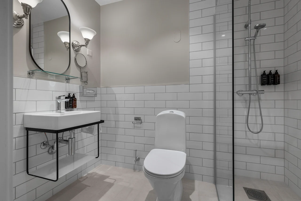 A clean and modern hotel bathroom with a white tiled shower, toilet, and sink area, designed for guest comfort.
