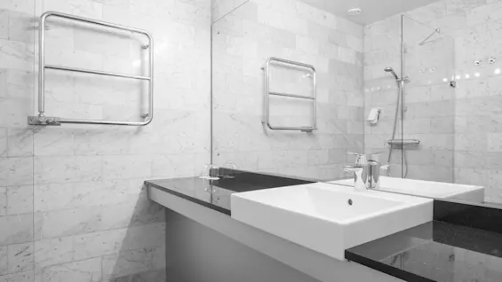 Modern hotel bathroom with marble tiles, a large mirror, a white sink on a dark countertop, and a towel warmer.