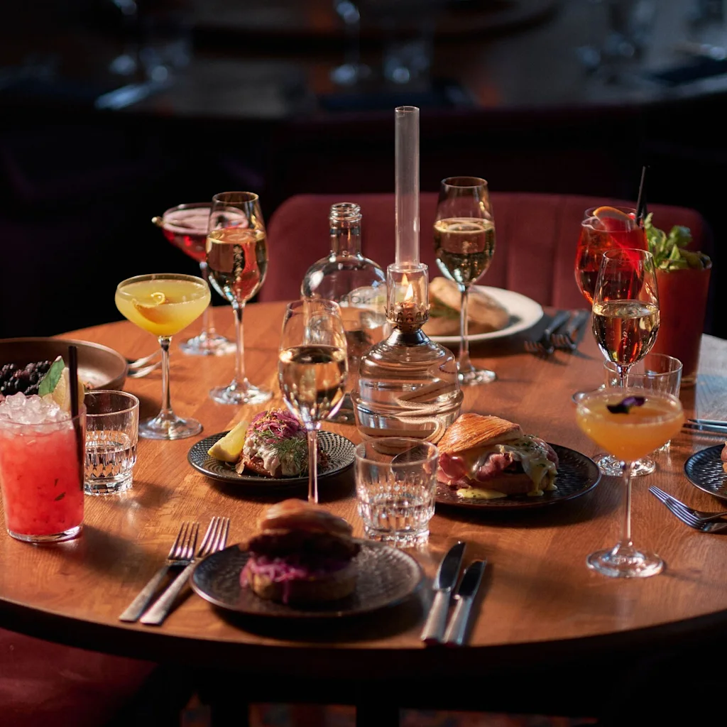 Ett mysigt bord på Clarion Hotel Post dukat med utsökt mat, cocktails och vin, upplyst av en varm lampa.