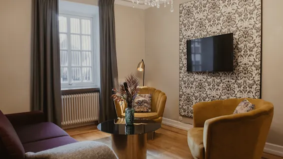 A cozy hotel lounge at Home Hotel Grand, Helsingborg, with a sofa, armchairs, and a TV, perfect for relaxation.