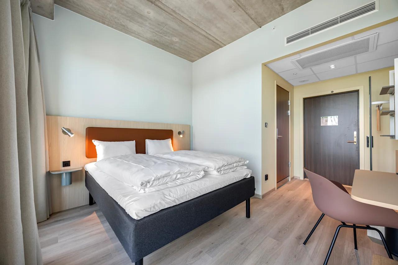 A modern and inviting hotel room with a comfortable bed, a small workspace, and warm lighting.