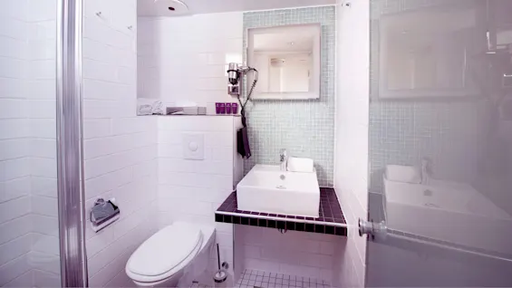A contemporary bathroom with white and blue tiles, featuring a toilet, sink, mirror, and a glass shower partition.