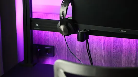 Quality Hotel Match. Hovedtelefoner hænger på en skærm med lilla baggrundsbelysning og en trævæg. Etiketten LUMEN synlig.