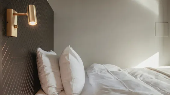 Ett mysigt och inbjudande hotellrum på Home Hotel Grand, Helsingborg, med en säng med vita lakan och en varm vägglampa.