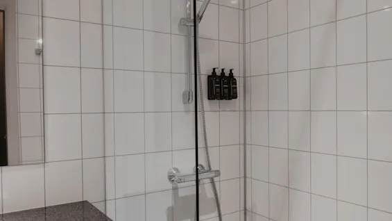 En lys og moderne bruser med hvide flisebelagte vægge, et elegant brusehoved og praktiske vægmonterede dispensere.