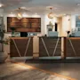 A stylish hotel reception area with three service desks, computers, and a decorative wall of books. A sign reads PRELUSA.