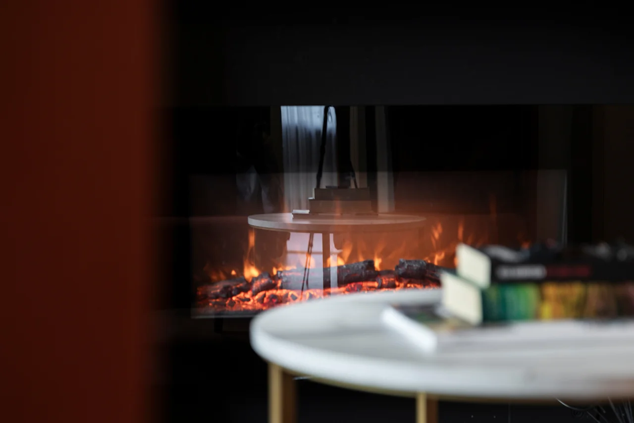 A cozy fireplace scene at Home Hotel Grand Bodø, with a table and books in the foreground, creating a warm ambiance.