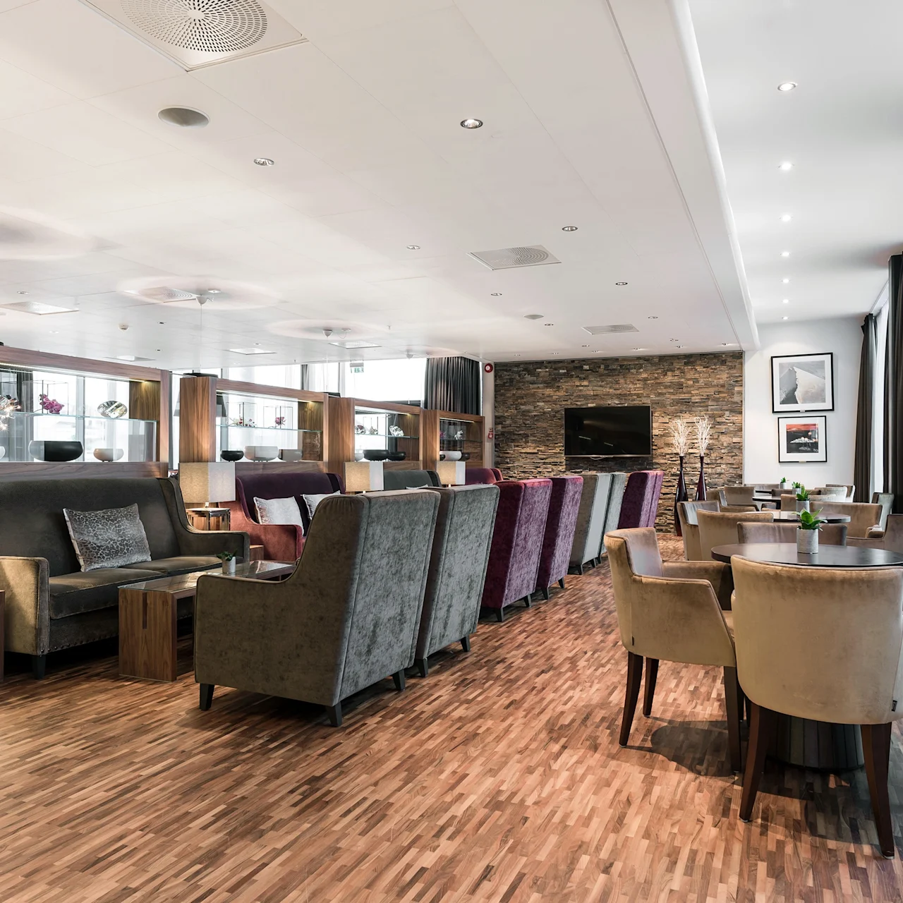 Elegant lounge med myke stoler og sofaer arrangert rundt trebord; plassert i en romslig, godt opplyst rom med tregulv og store vinduer med lette gardiner.