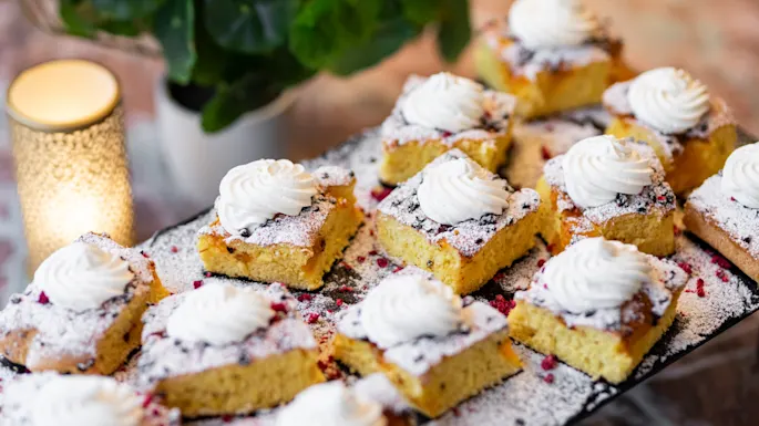 Delicious square cakes topped with whipped cream, powdered sugar, and red sprinkles, ready to be enjoyed at a cozy gathering.