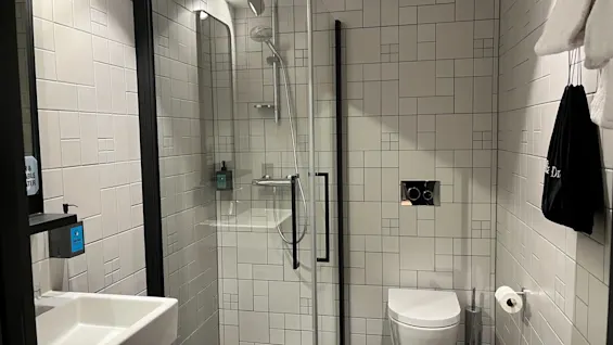 Valoisa, moderni kylpyhuone, jossa on suihku, wc ja pesuallas. Seinälle asennetussa annostelijassa lukee ABLE TER.