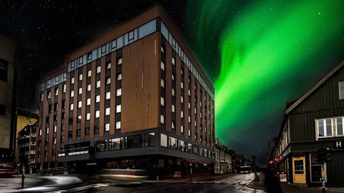 Night scene with a building labeled THE EDGE under a vibrant aurora borealis, street with light trails, and a person walking. 