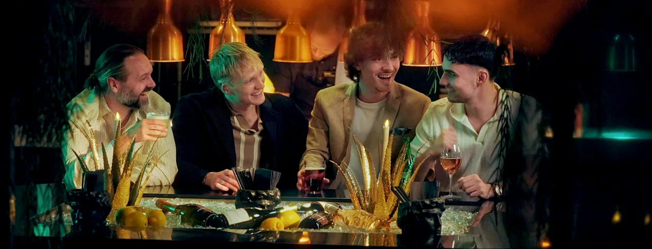 Fyra personer umgås och njuter av drinkar i en bar, delar skratt och samtal i en varm, inbjudande atmosfär.