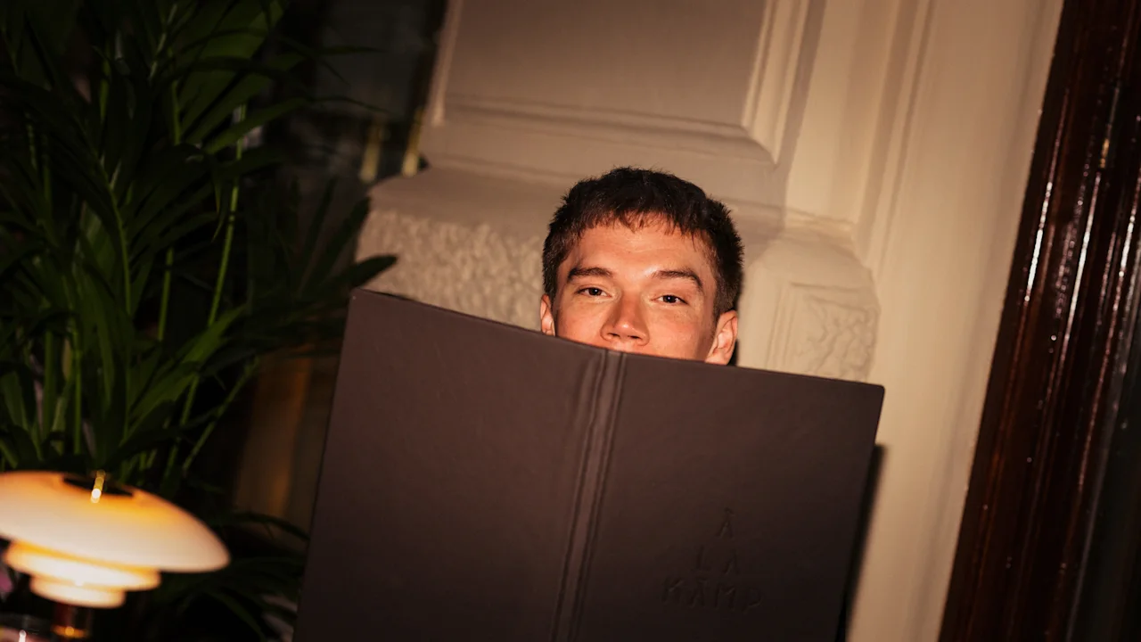 Person ser over en meny på Hotel Kämp – Restaurant À La Kämp. Menyen leser A LA KAMP.