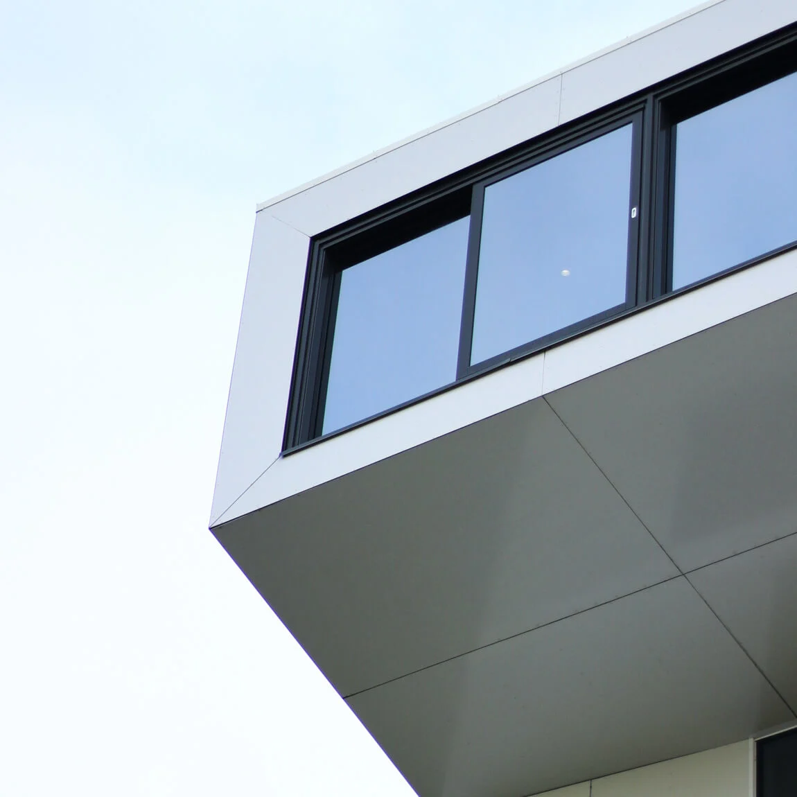 En moderne bygning stikker ut med store glassvinduer, strekker seg inn i en skyet himmel. Bygningens stilrene design har rene linjer og en minimalistisk estetikk.