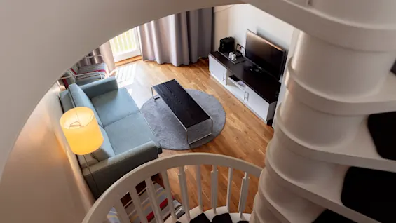 Et moderne opholdsrum med en lyseblå sofa, sofabord og TV, set fra toppen af en hvid vindeltrappe.