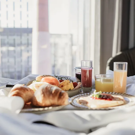 Nyt en deilig frokost på sengen med ferske bakverk, frukt og juice, med utsikt over en bysilhuett.