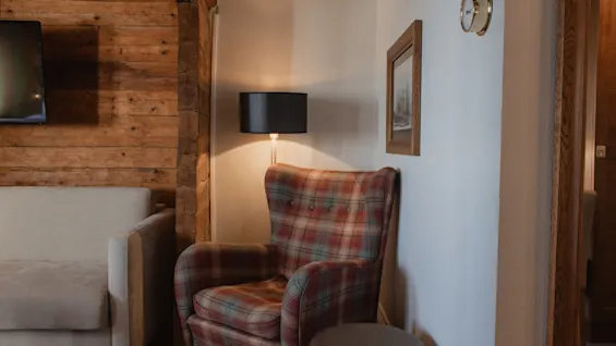 Et indbydende rum med en komfortabel ternet lænestol badet i varmt lampelys, ved siden af en rustik trævæg og en sofa.