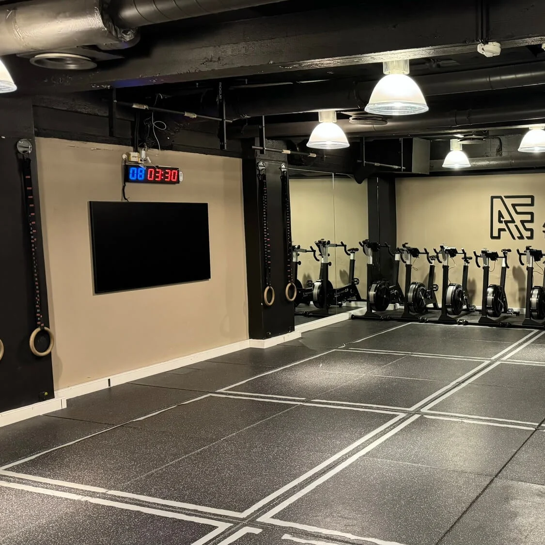 Rivi kuntopyöriä kuntosalilla, seinällä digitaalinen kello ja logo "ÆRA TRAINING".