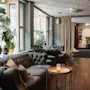 En varm och inbjudande hotellounge med plyschsoffor, stora fönster och frodiga gröna växter, som leder till en bar.