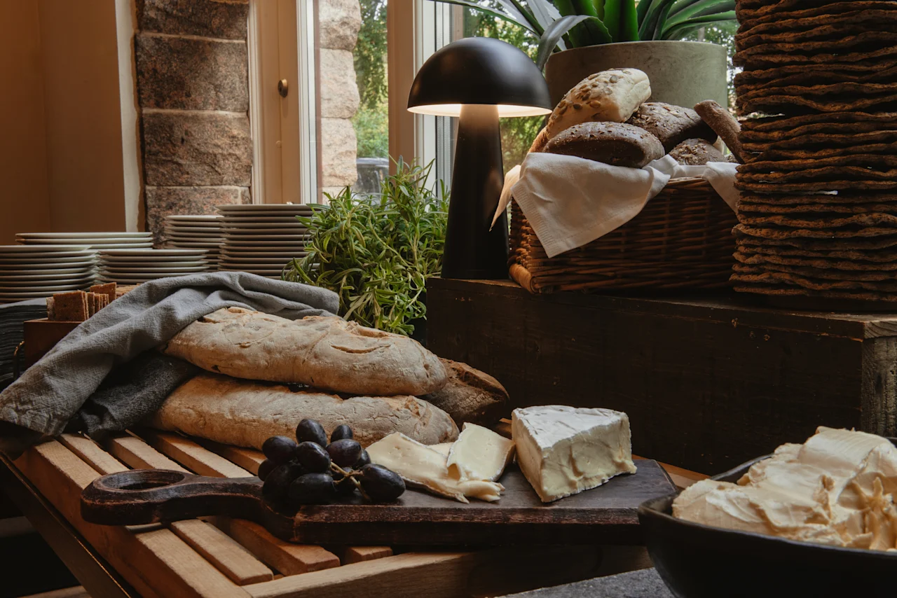 En lækker morgenmadsbuffet på Home Hotel Norre Park i Halmstad, med frisk brød, oste, druer og stablede tallerkener.