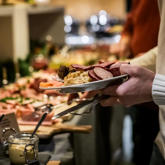 En person håller en tallrik fylld med pålägg och köttbullar vid en julbordsbuffé.