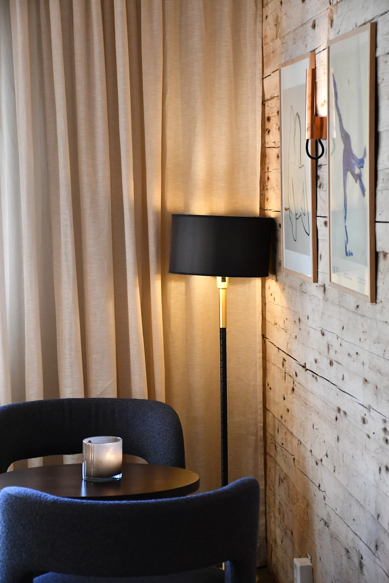 Et varmt og indbydende hjørne med blød belysning, to komfortable stole, et lille bord med et tændt lys og indrammet kunst på en rustik trævæg.