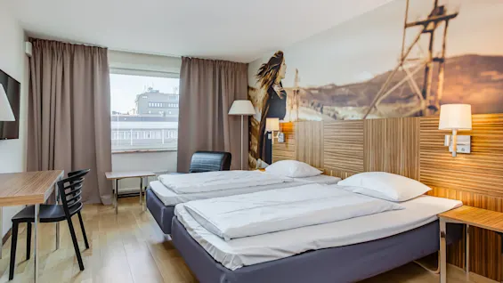 Hotellihuoneessa on kaksi siististi pedattua erillistä vuodetta, seinävalaisin ja seinämaalaus. Raskailla verhoilla varustetusta ikkunasta näkyy kaupunkimaisema.