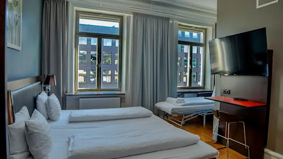Ett bekvämt hotellrum med en stor säng, en extrasäng, en TV och fönster med utsikt över en stadsbyggnad.