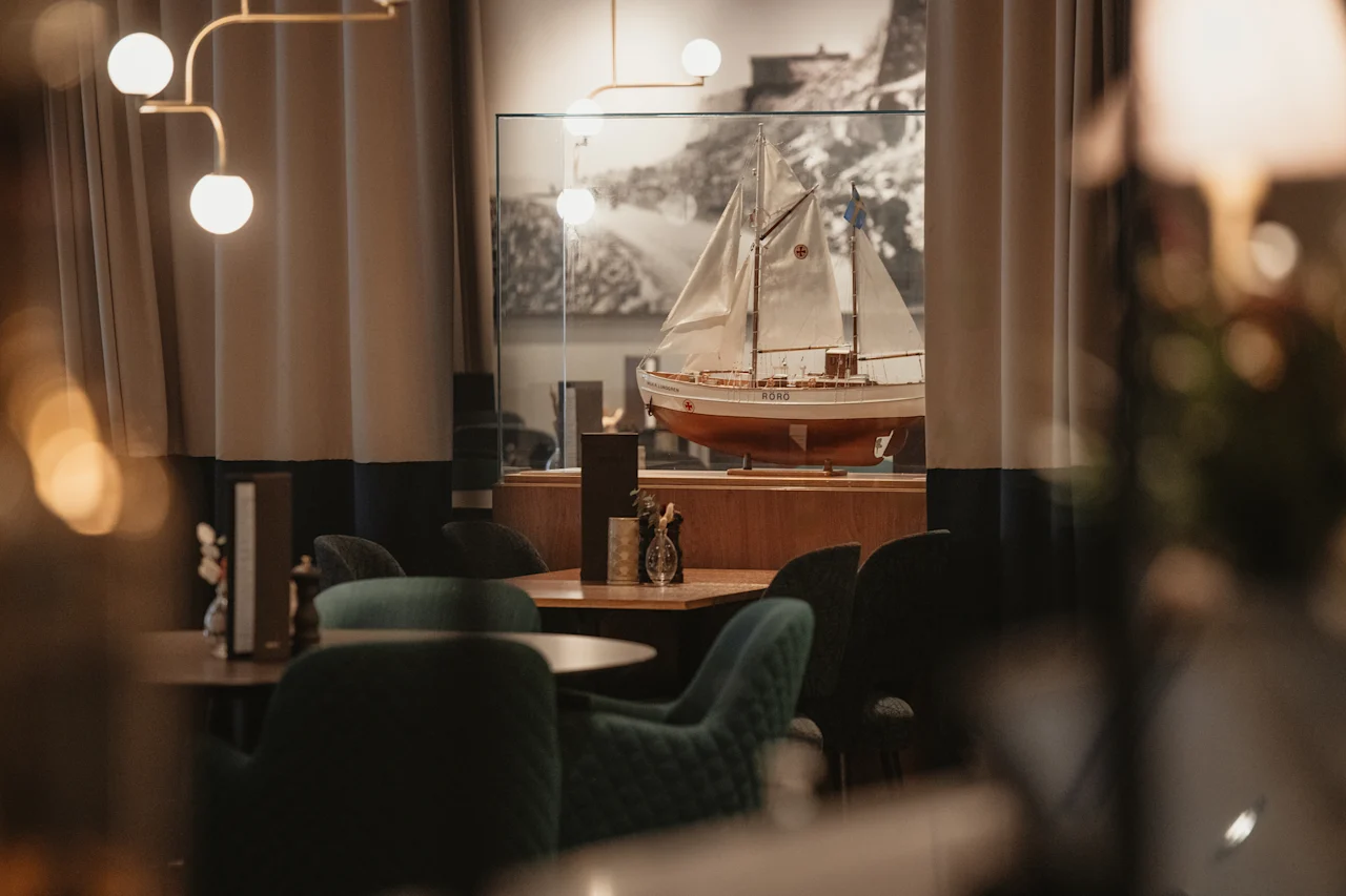 En varm og indbydende restaurant eller lounge med komfortable siddepladser, med en fremtrædende udstilling af en modelsejlbåd ved navn NORD.