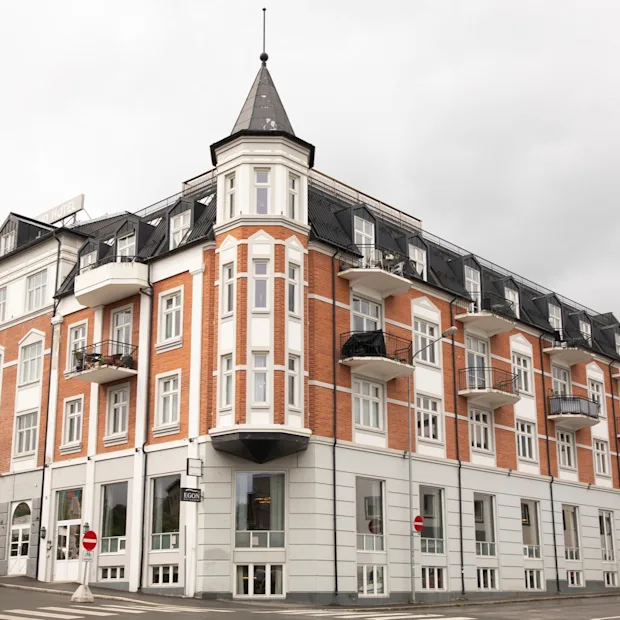 En storslået bygning med murstens- og hvid arkitektur, med et fremtrædende hjørnetårn og altaner, beliggende langs en gade.