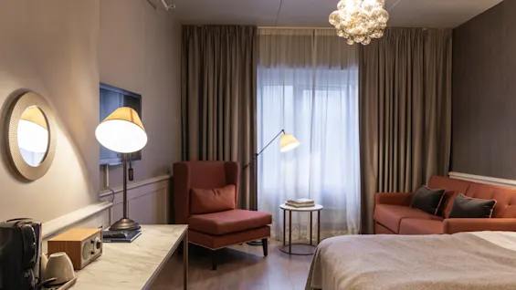 A warm and inviting hotel room at Home Hotel Grand Bodø, featuring comfortable seating, a workspace, and soft lighting.