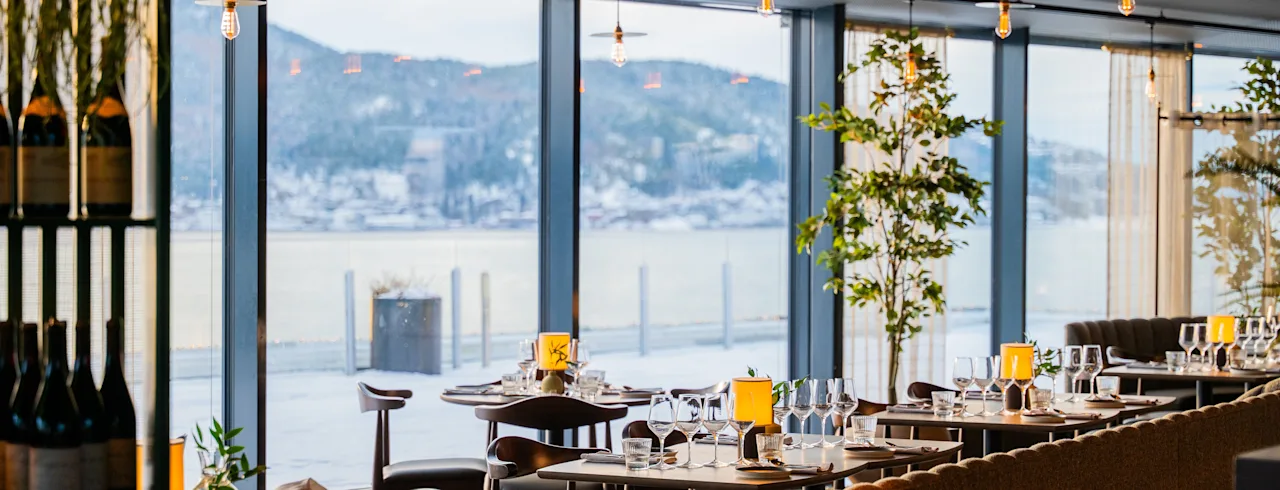 En elegant spisesal med dekkede bord og et fantastisk vinterlandskap synlig gjennom store vinduer.