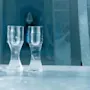 To isglas står på et isbord i et frostet rum, omgivet af isvægge og en isskulptur i baggrunden.