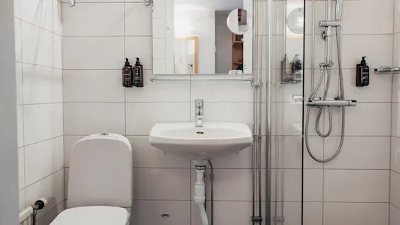 Ett rent, modernt badrum med vita kaklade väggar, toalett, handfat med spegel och dusch med glasvägg.