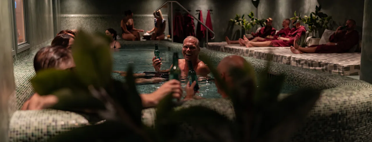 Ihmiset nauttivat rentouttavasta hetkestä hämärästi valaistussa kylpyläaltaassa, jotkut pitävät juomia, toiset rentoutuvat lähellä.