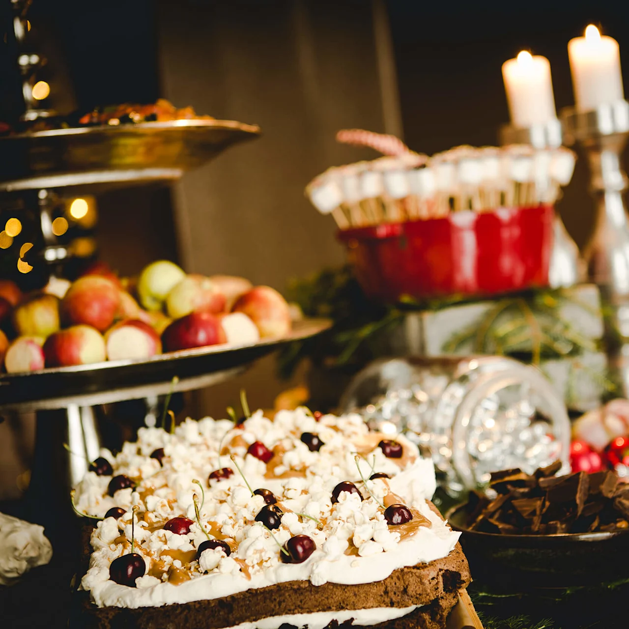 A festive table with assorted desserts, candles lit, creating a warm ambiance, blurred bokeh lights in the background.