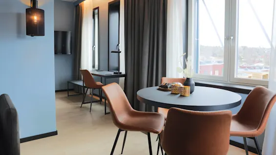 A contemporary room with a round table, leather chairs, curtains, and a view of the exterior.